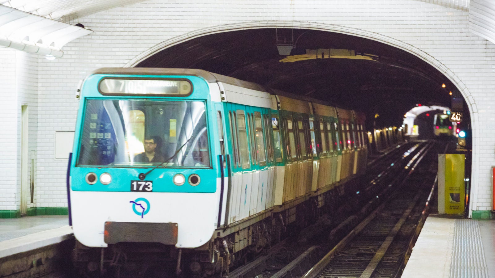 Turquoise and white metro train arriving at an underground station as another train approaches in the opposite tunnel.