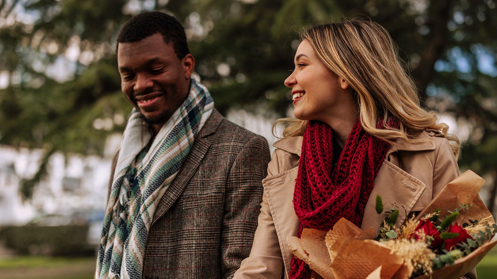 Two people walking outdoors together, with one carrying a bouquet of flowers.