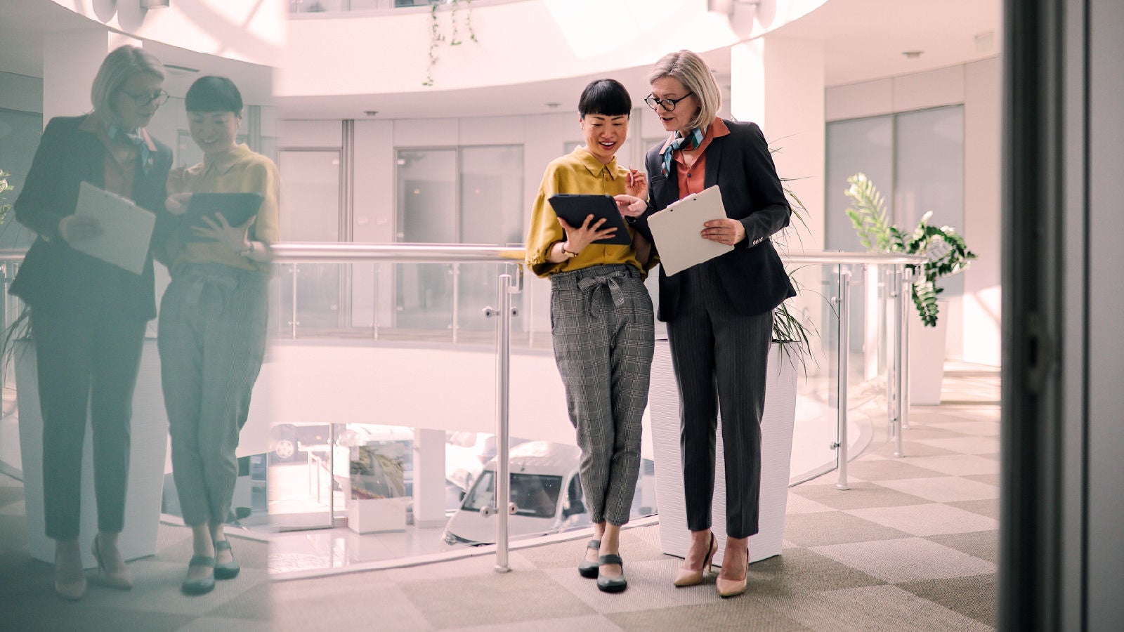 Two business professionals reviewing a tablet together in a modern office hallway with natural light.