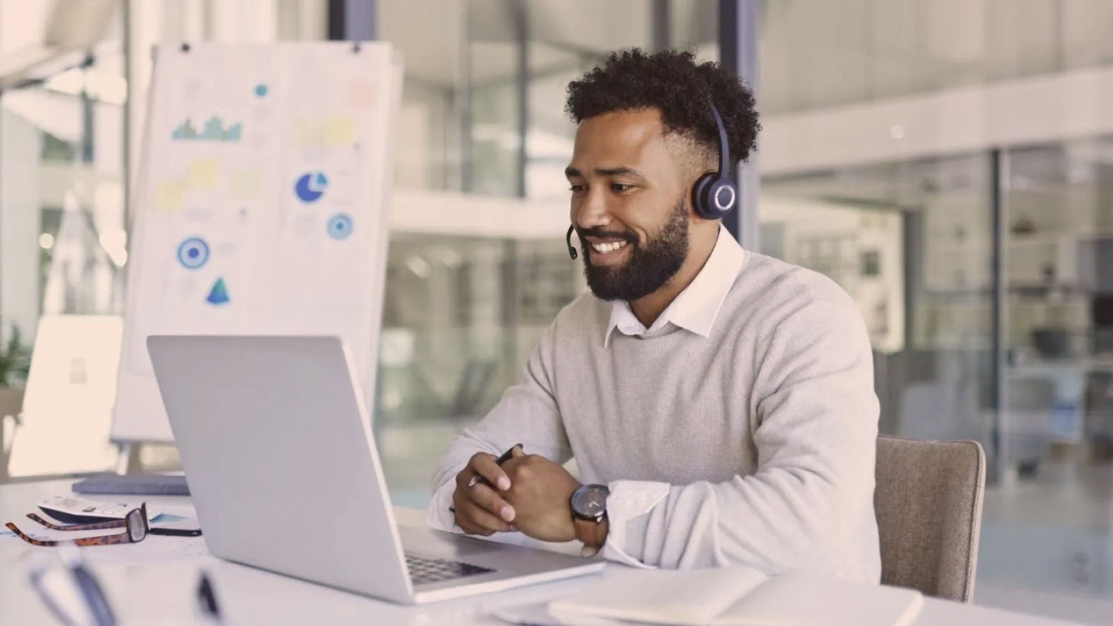 Professional wearing a headset while participating in a video call on a laptop in an office.