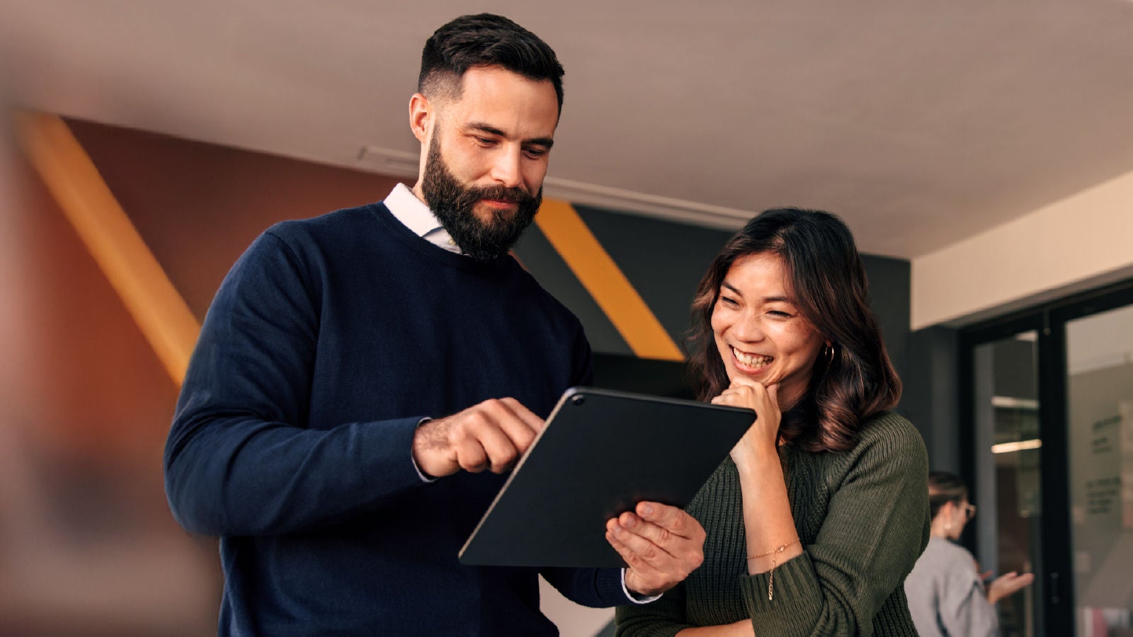 A man showing a woman something on a tablet as they collaborate in a bright, modern office.