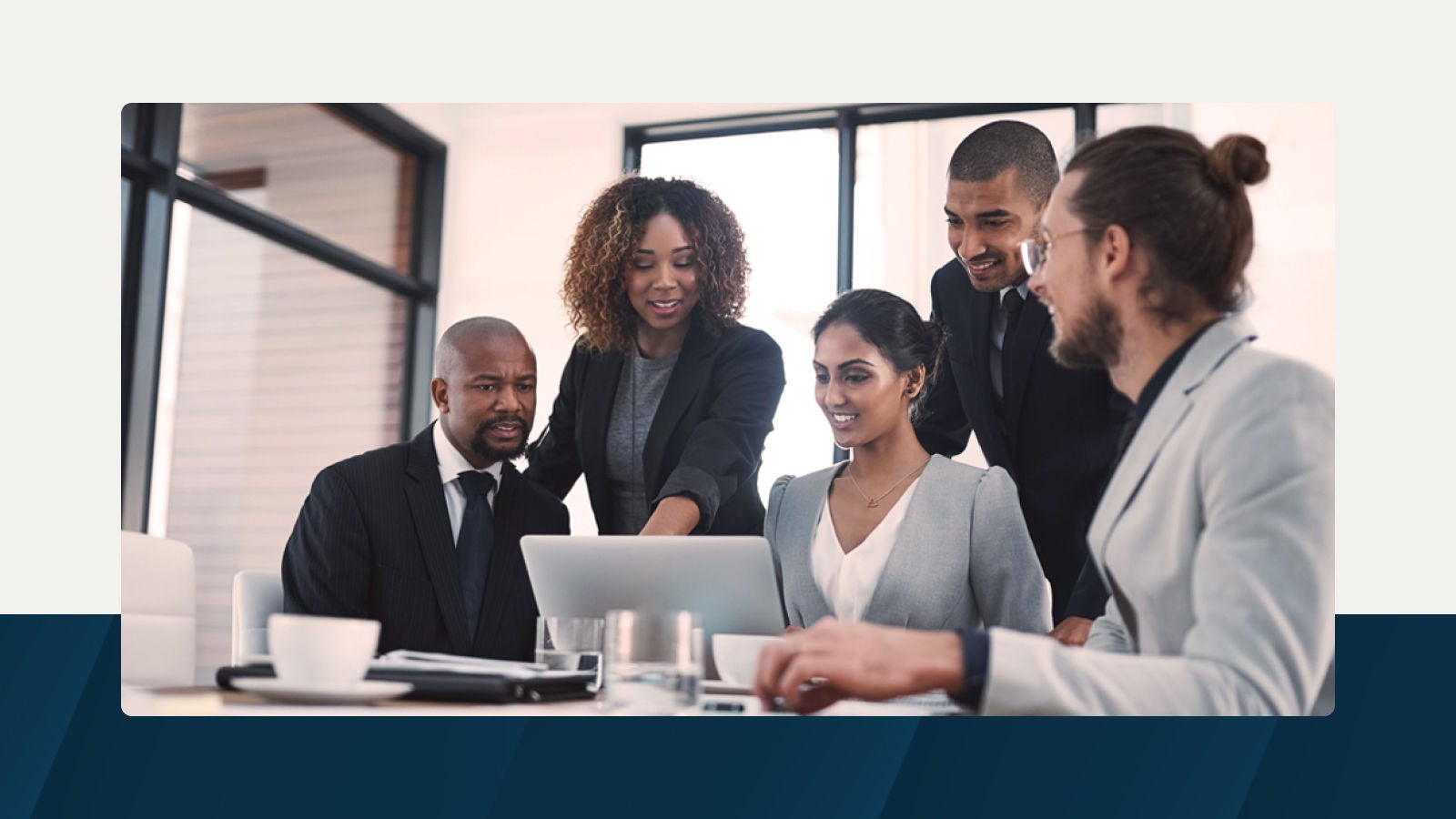 A group of business professionals collaborating around a laptop in a modern office setting, engaged in a discussion on data-driven decision-making.