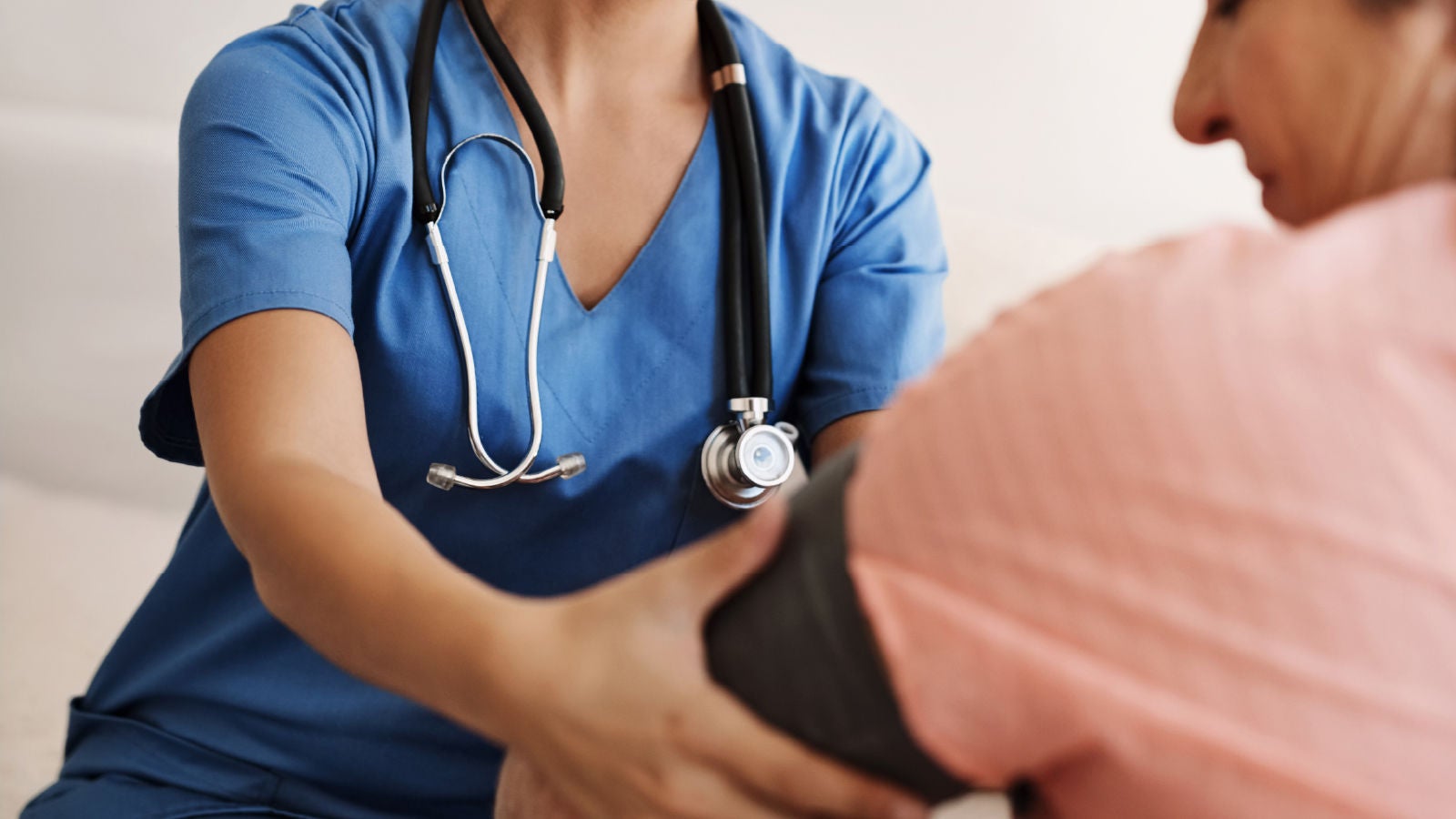 Image showing a healthcare worker in blue scrubs with a stethoscope taking a patient’s blood pressure.