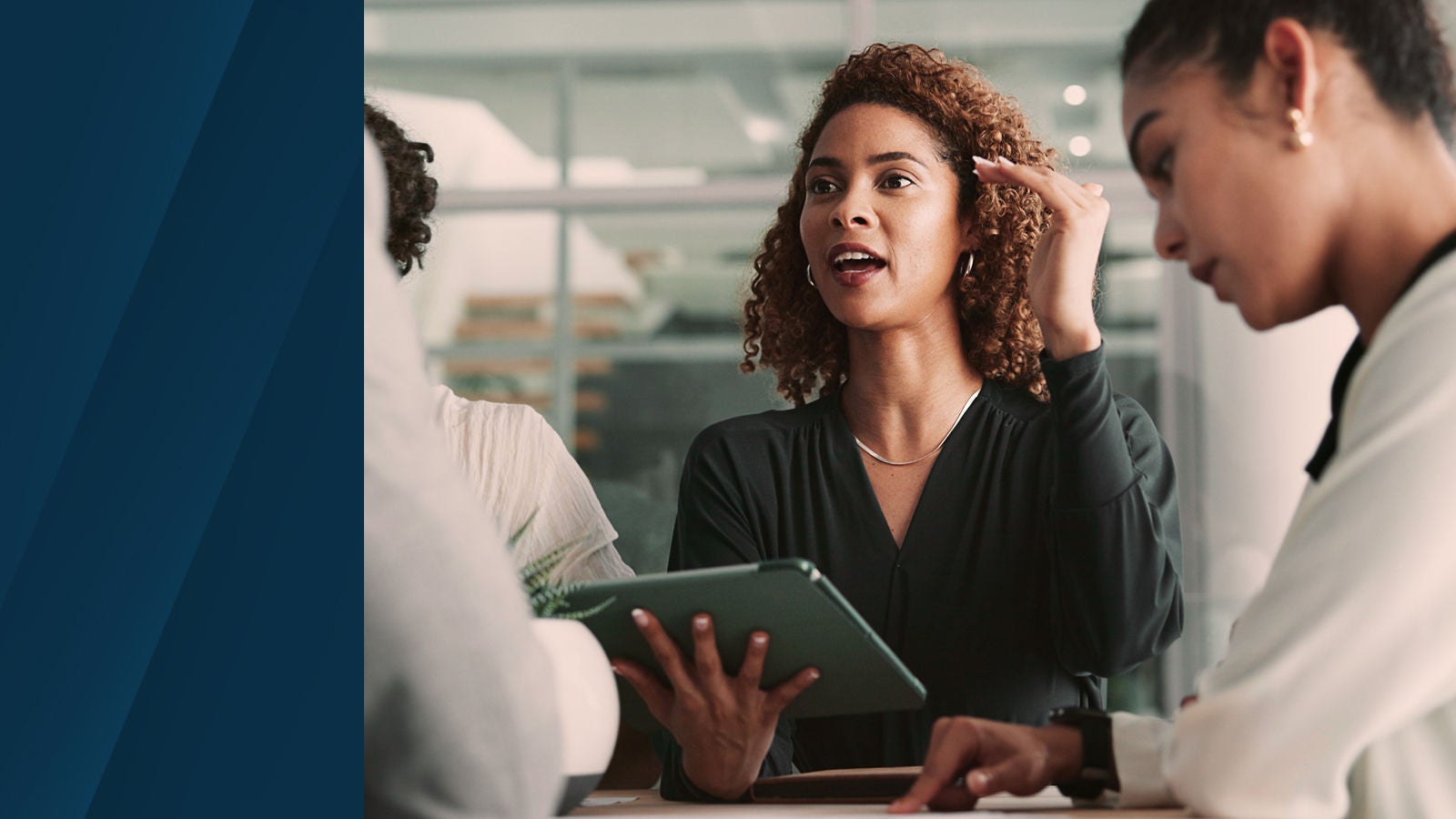Three professionals collaborating around a table while reviewing information on a tablet in an office setting.