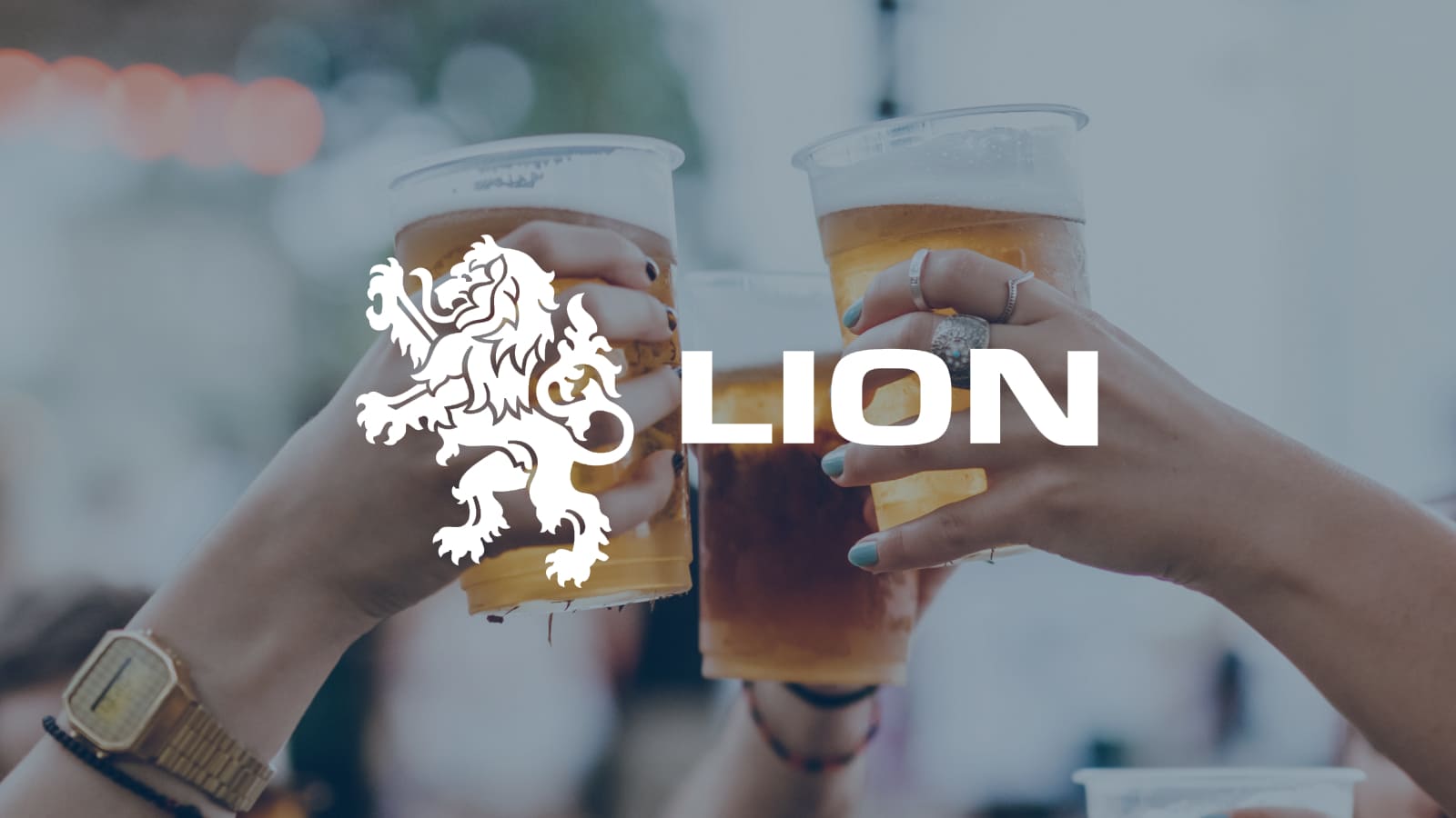 Lion Logo displayed center. Several people holding and clinking glasses of beer in an outdoor setting.