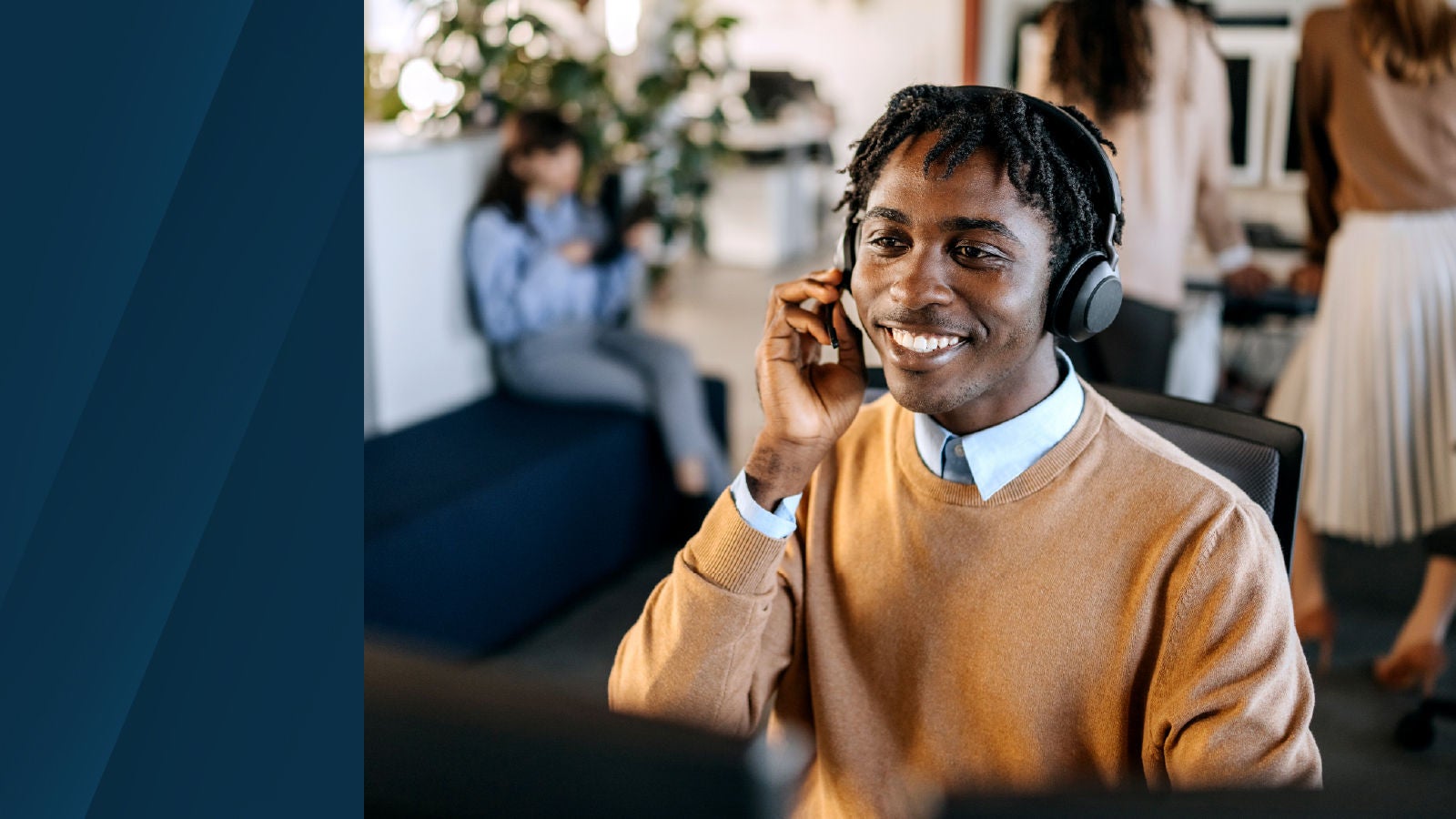A customer service agent wearing a headset smiles while speaking on a call in a modern office environment, with colleagues working in the background.