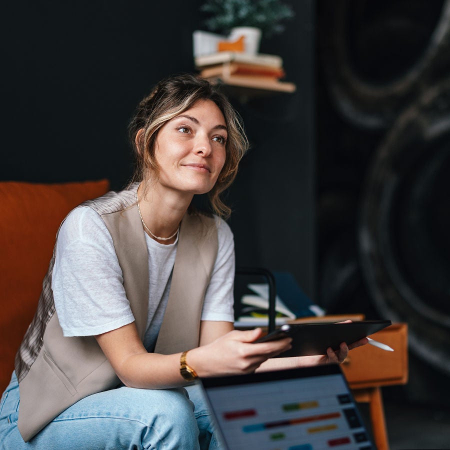 A woman comfortably sitting on a couch, with a tablet on her hand