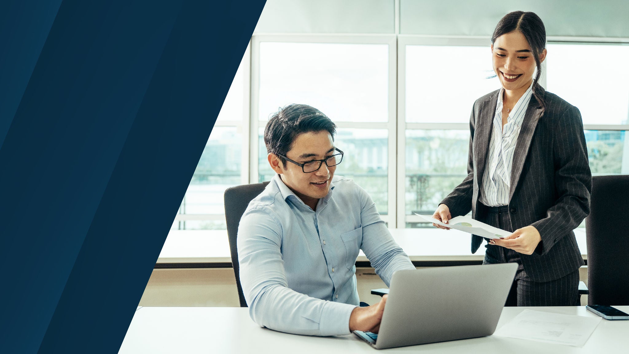 オフィス環境でノートパソコンを使用し、資料を共有しながら作業するビジネスパーソン。