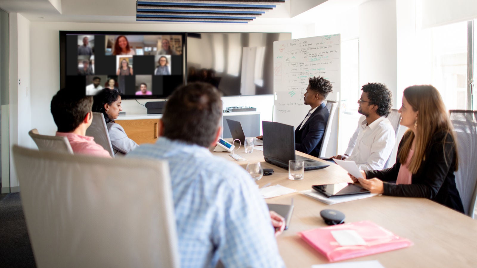 Team members in a conference room joining remote participants on a video call.