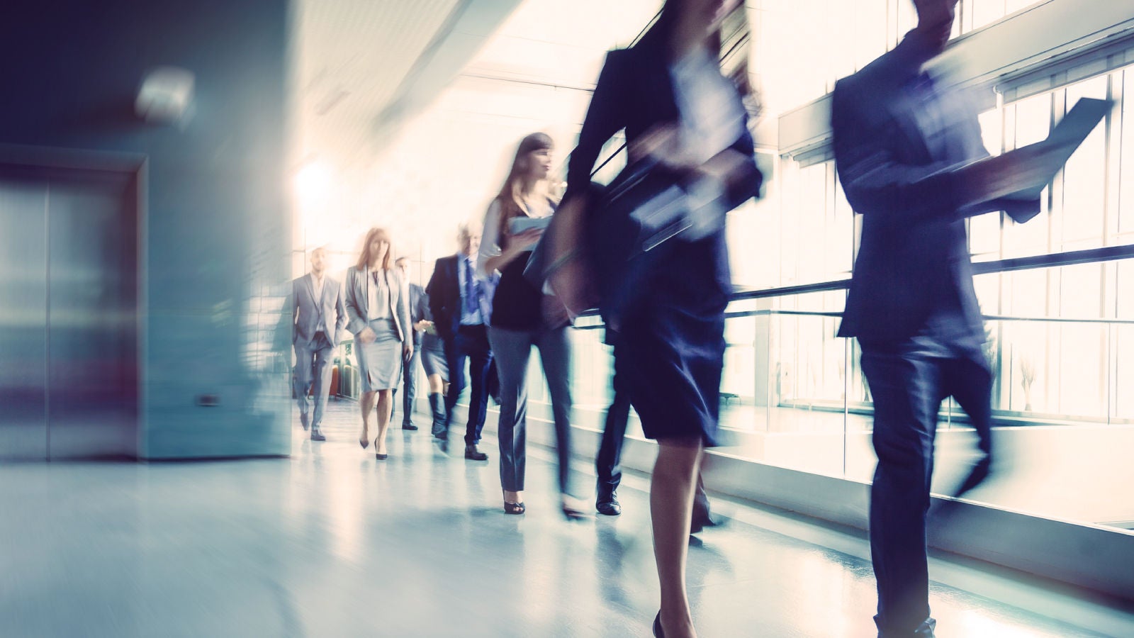 A blurred image of business professionals walking in a modern office hallway