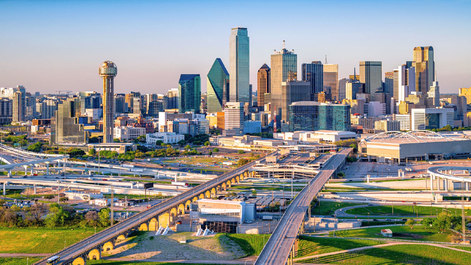 Aerial view of the Dallas skyline with highways, bridges, and city buildings during daylight.