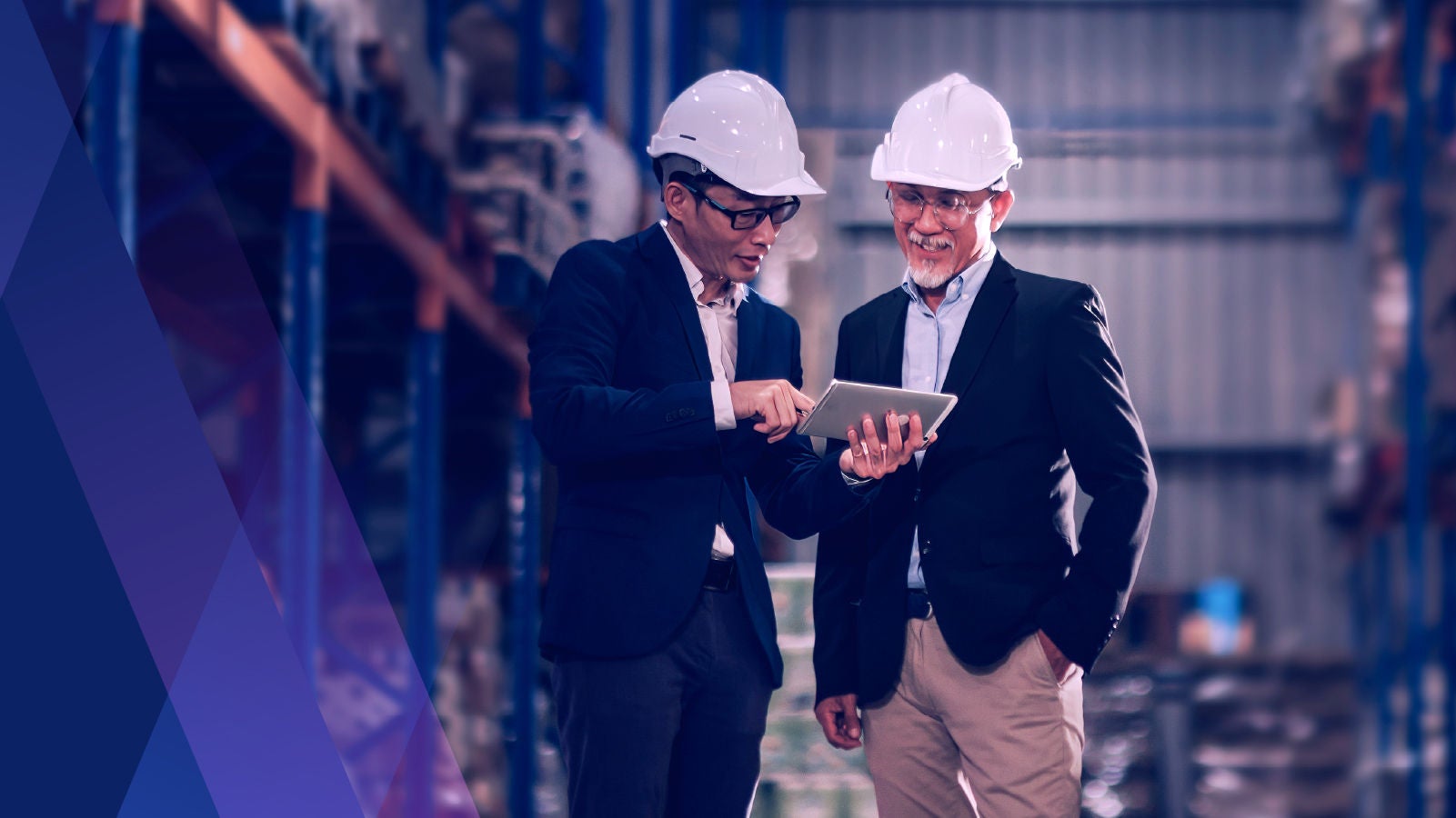 two men in hard hats in a warehouse looking at a tablet