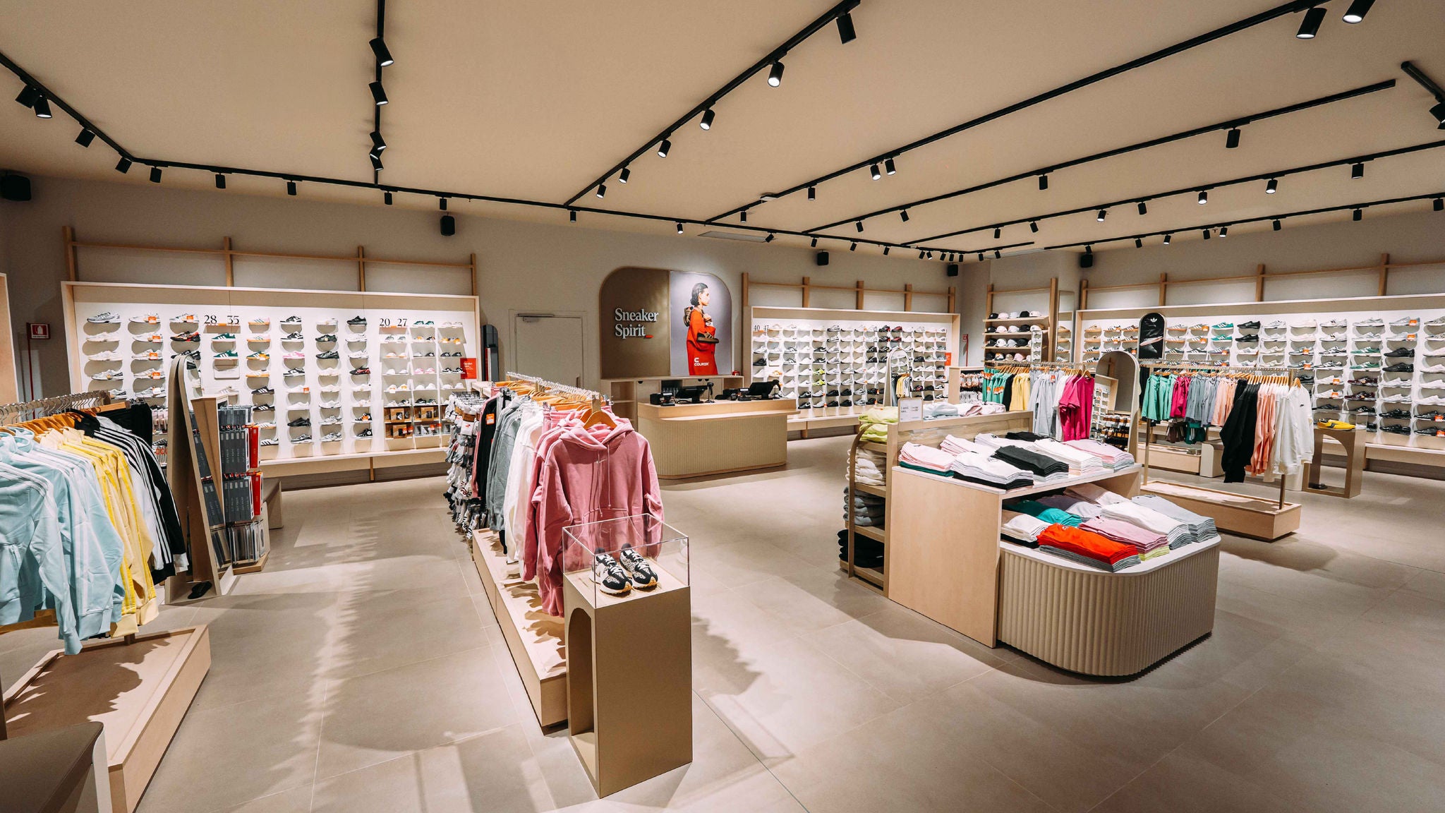 Modern retail sneaker and apparel store interior with clothing racks, shoe displays, and overhead lighting.