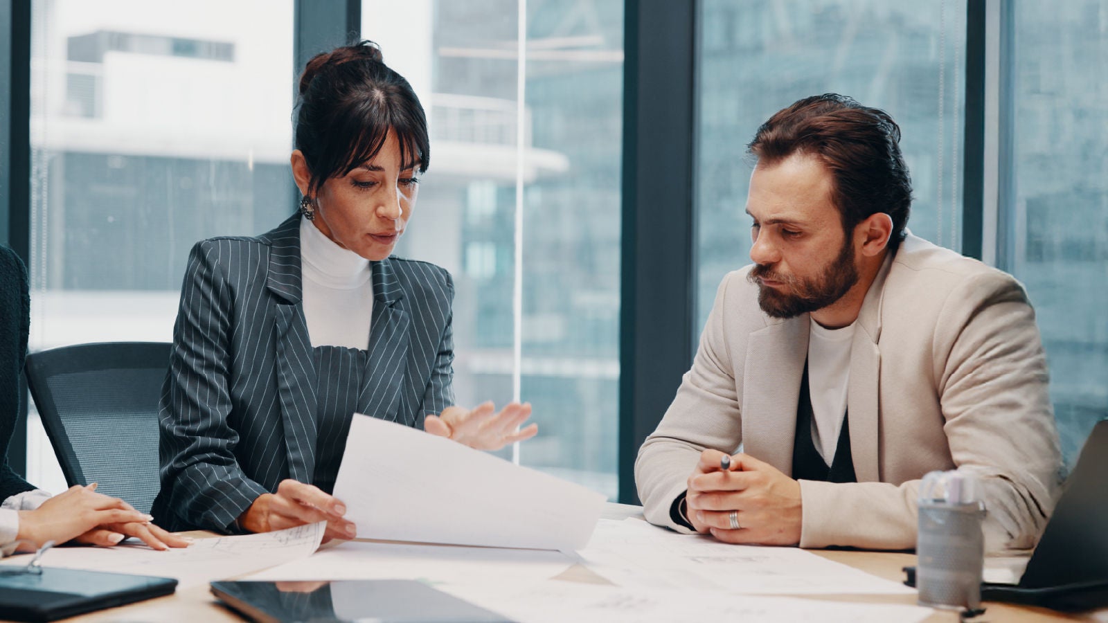 A woman and a man seated at a conference table analyzing paperwork and financial reports in a bright office setting.