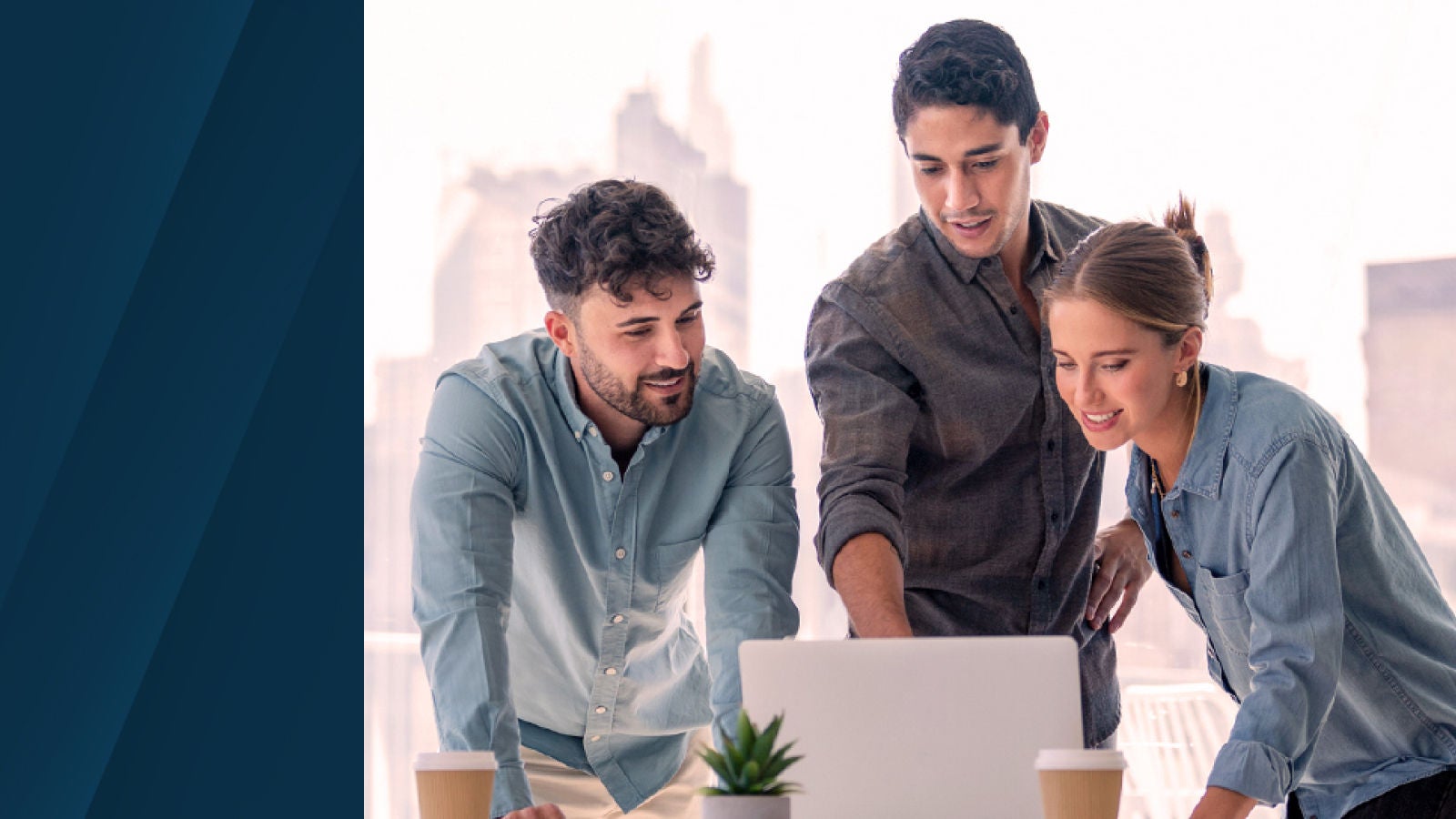 A group of three colleagues collaborate at a table, looking at a laptop screen. They appear engaged in discussion, with one person pointing at the screen. The background shows a bright office space with a cityscape view.
