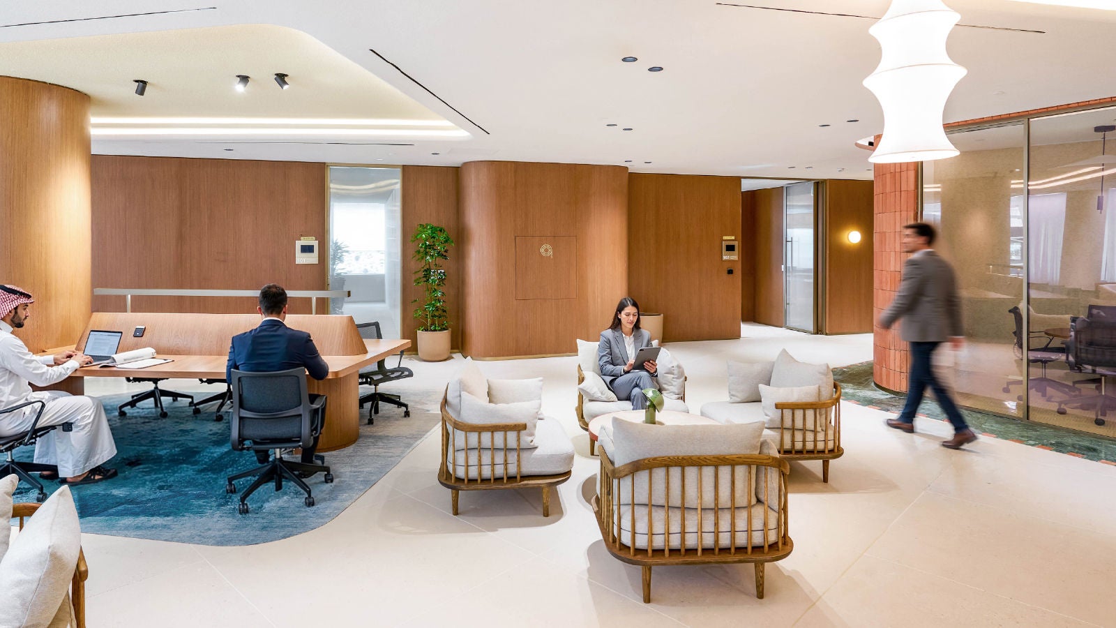Modern Executive Centre office lounge with professionals working at tables, using a tablet, and walking through the space.