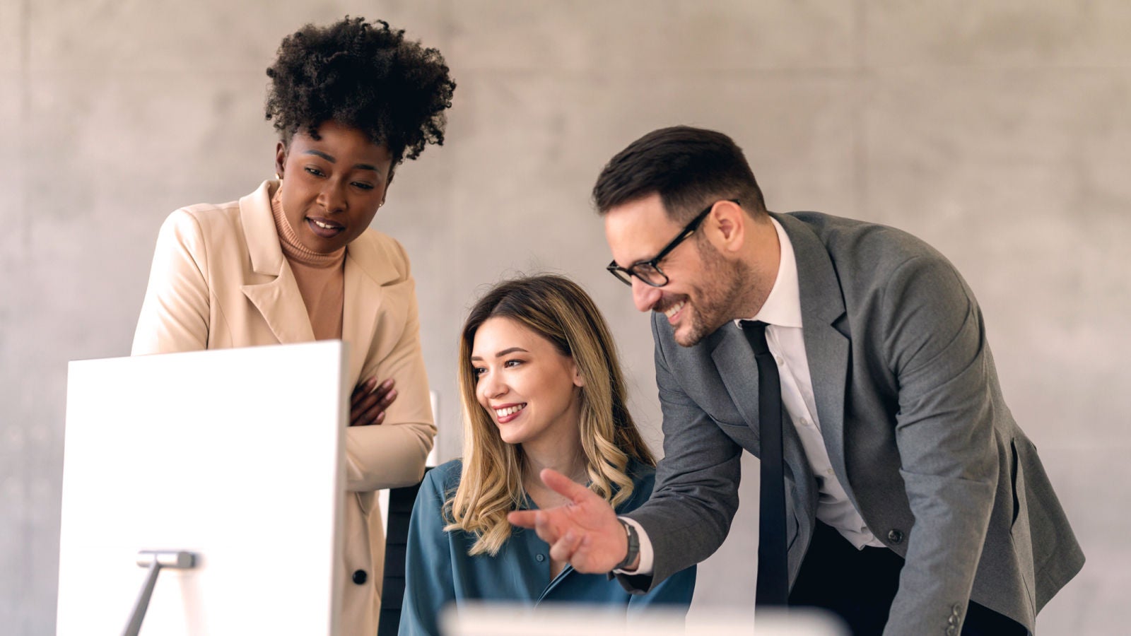 Three professionals smiling while working together at a desktop monitor in a modern office, representing collaboration and digital planning.