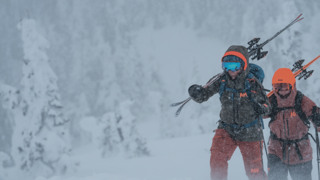 Two people carrying skis up a snowy hill