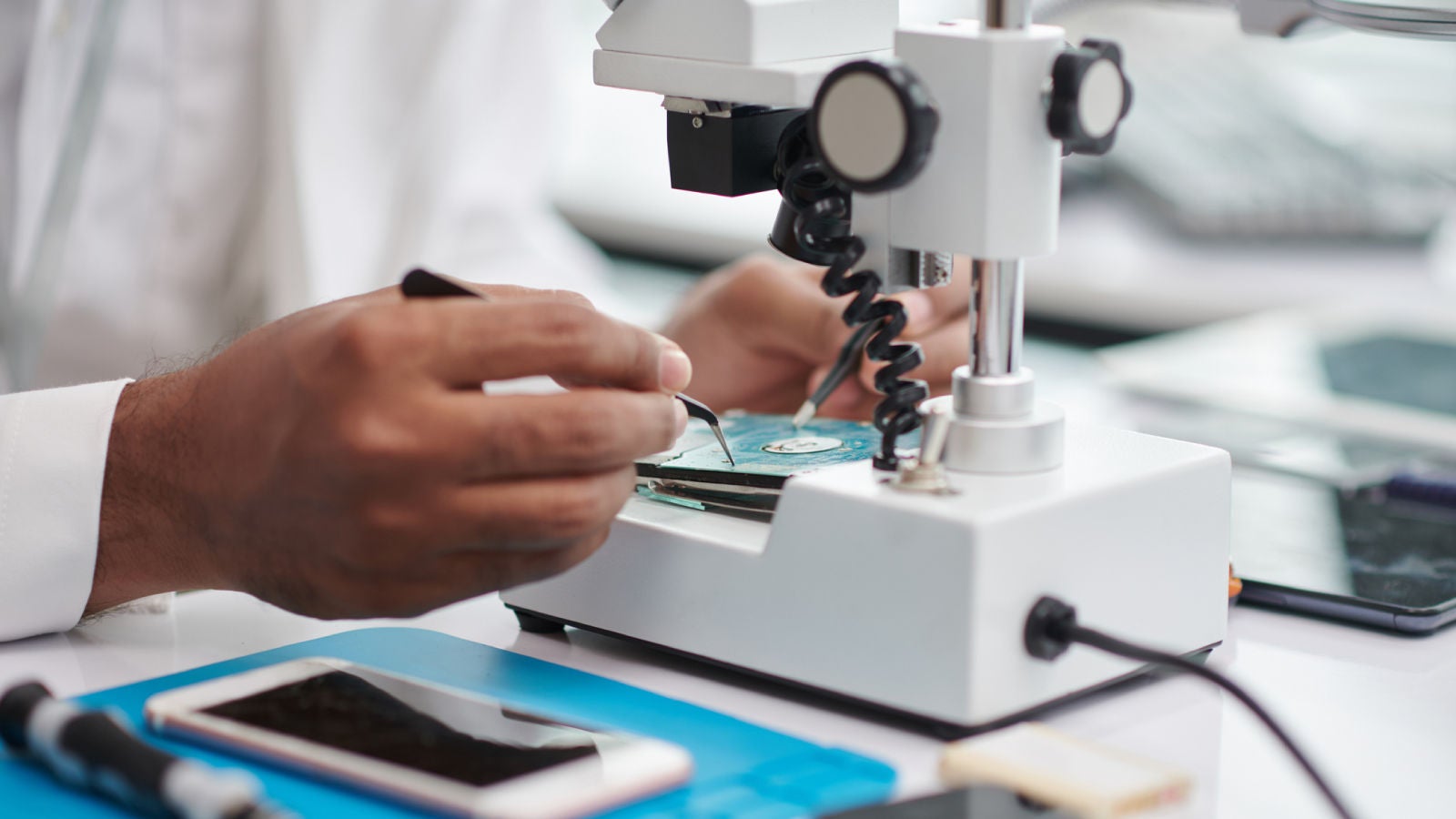 Close-up of a technician repairing a circuit board under a microscope.