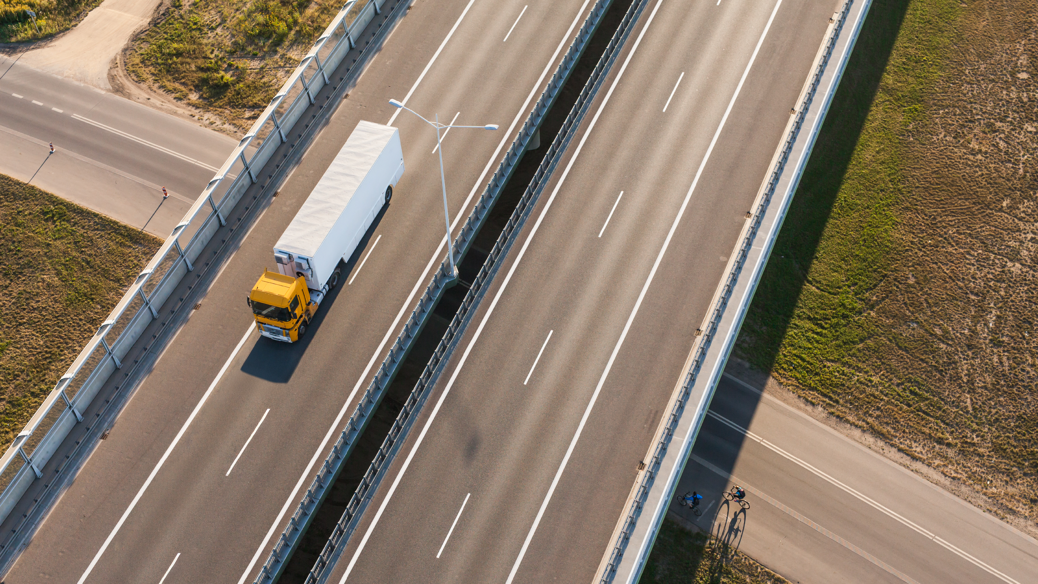 An aerial view of a cargo truck driving on a divided highway surrounded by open roads and greenery.