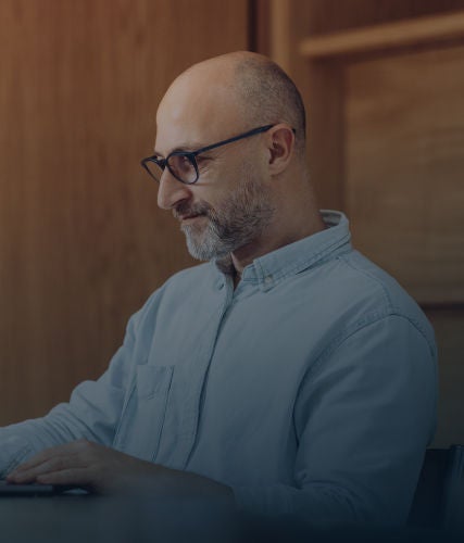 Close-up profile of a man with glasses and a beard typing on a laptop.