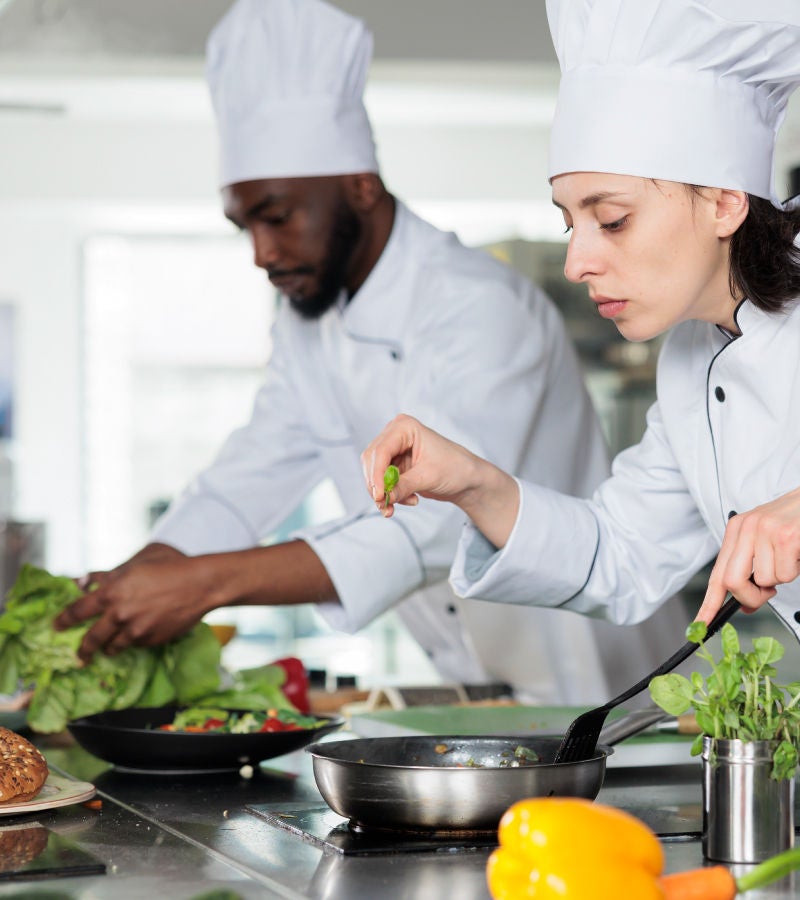 Two chefs in white uniforms preparing food in a professional kitchen.