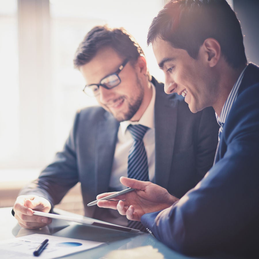 Two professionals in formal attire reviewing information on a tablet, indicating collaboration and business strategy.