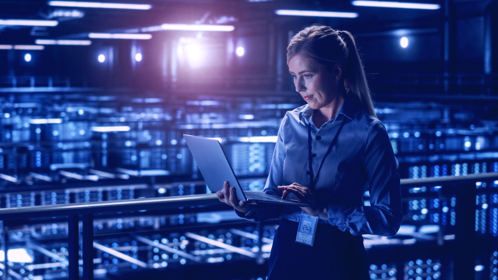 Woman checking her laptop while working in a server room.