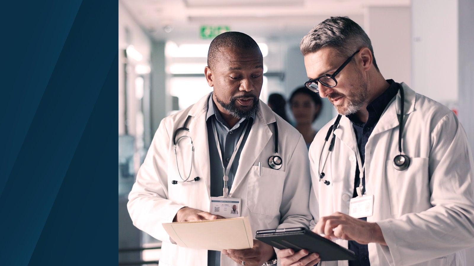 Two doctors in lab coats and stethoscopes reviewing patient data on a tablet in a hospital setting, representing collaboration in healthcare financial planning.