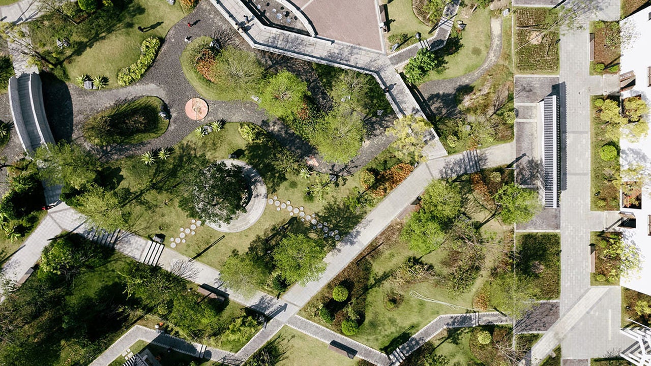 Aerial view of a landscaped park with winding paths, trees, and seating areas.