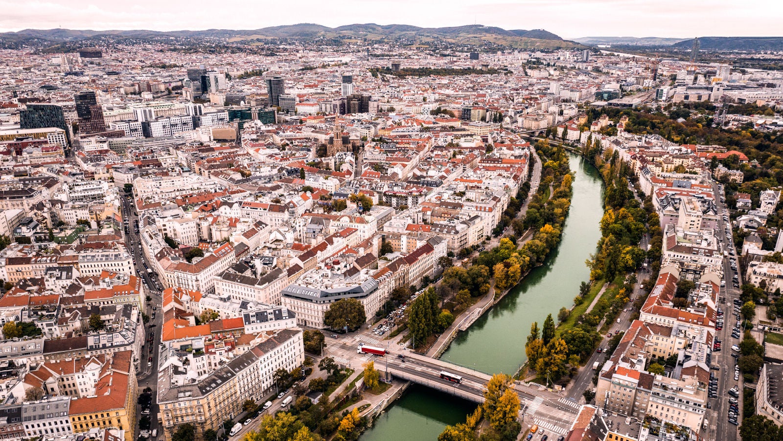 Aerial view of Vienna cityscape with dense buildings, a river running through the city, and bridges connecting both sides.