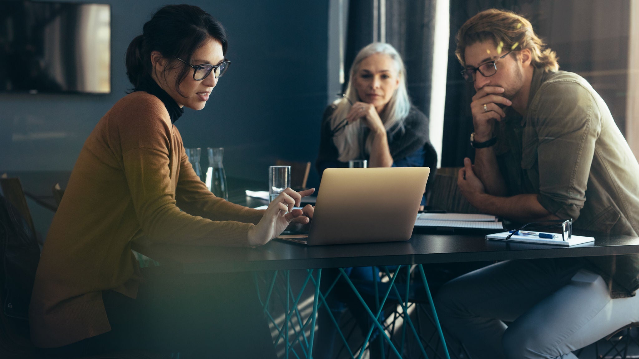 Three coworkers sitting at a table looking at a laptop
