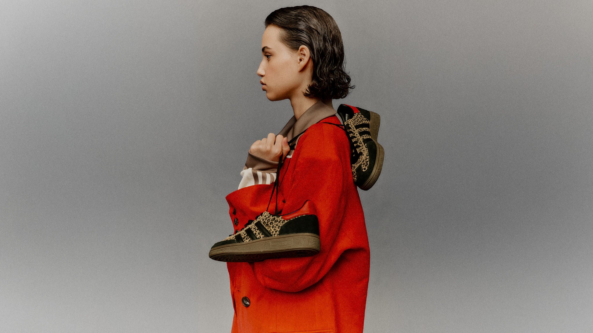 Woman in a red coat holding patterned sneakers against a gray background.