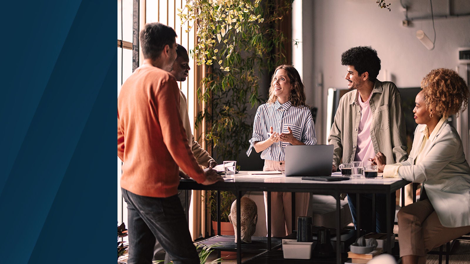 Team of professionals collaborating and smiling around a conference table in a modern office with natural light and plants.