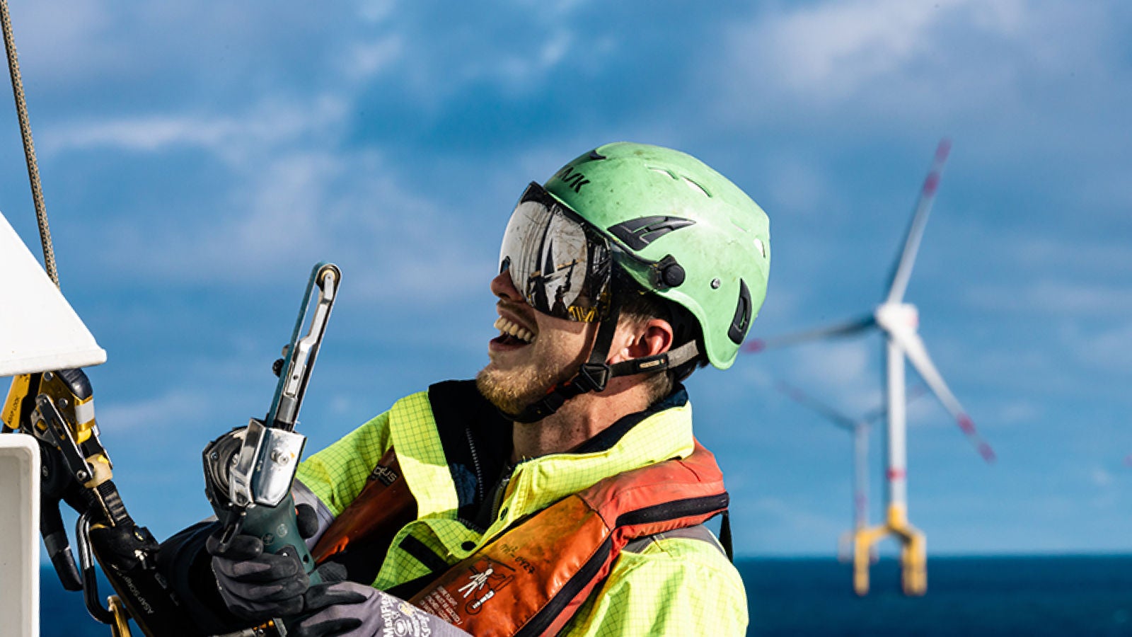 Eine Person mit Schutzhelm, Handschuhen und Brille, die an einem Windrad arbeitet 