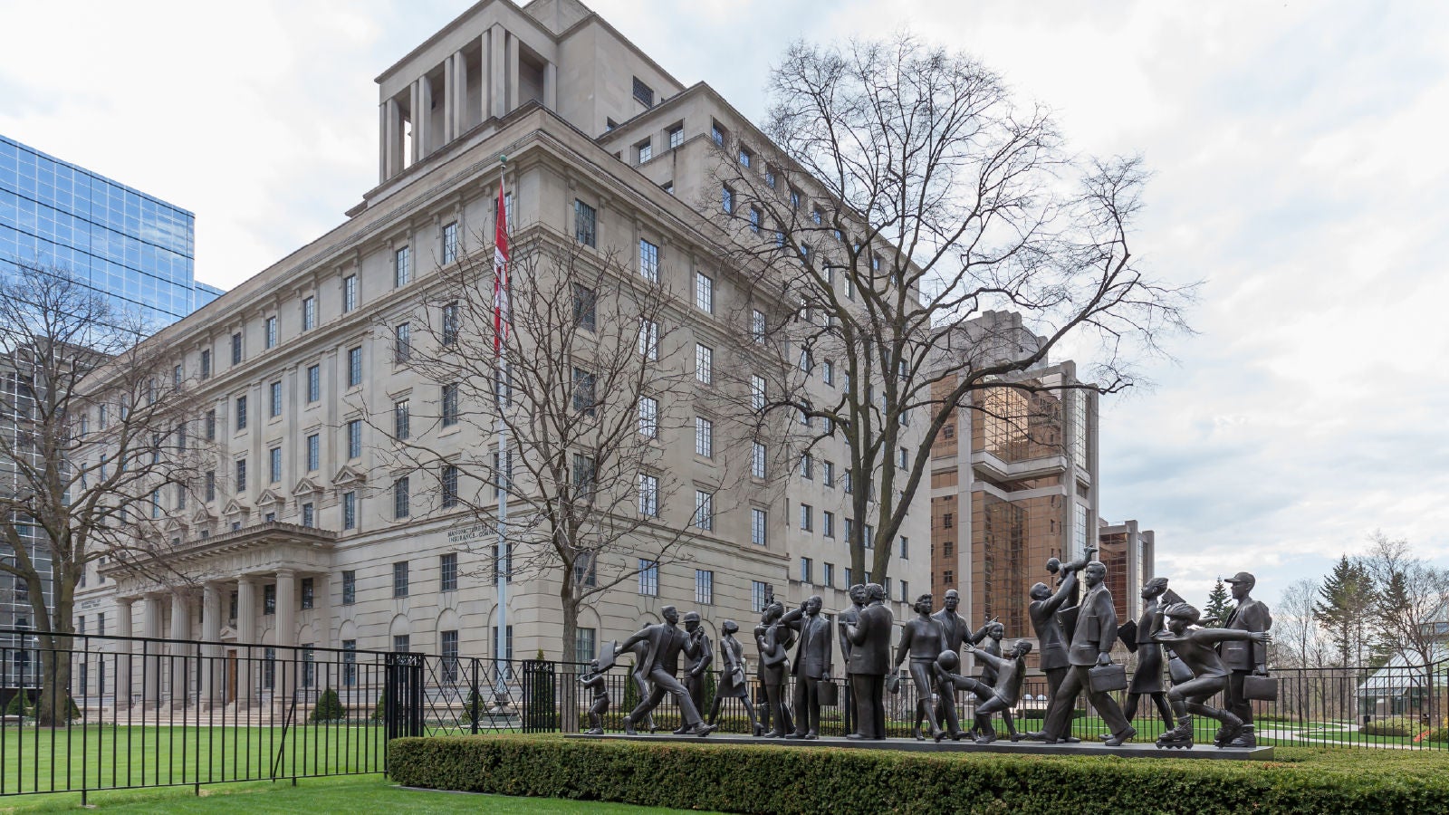 A government-style building with a Canadian flag and a sculpture of people in front of it.