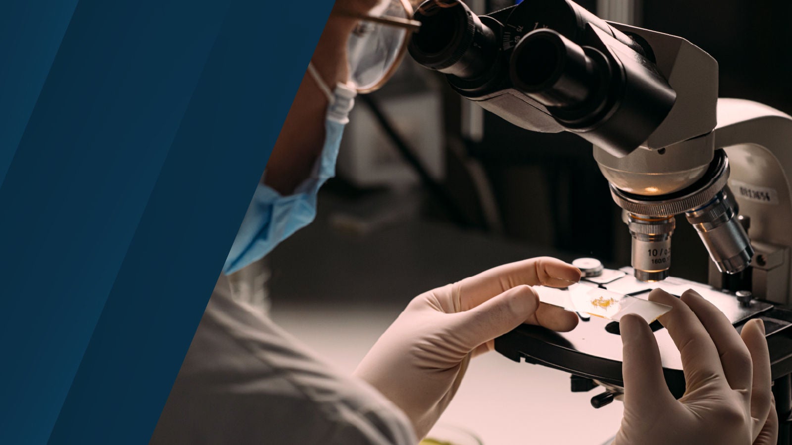 Close-up of a scientist in protective gear placing a slide under a microscope, with soft lighting and laboratory instruments in the background.