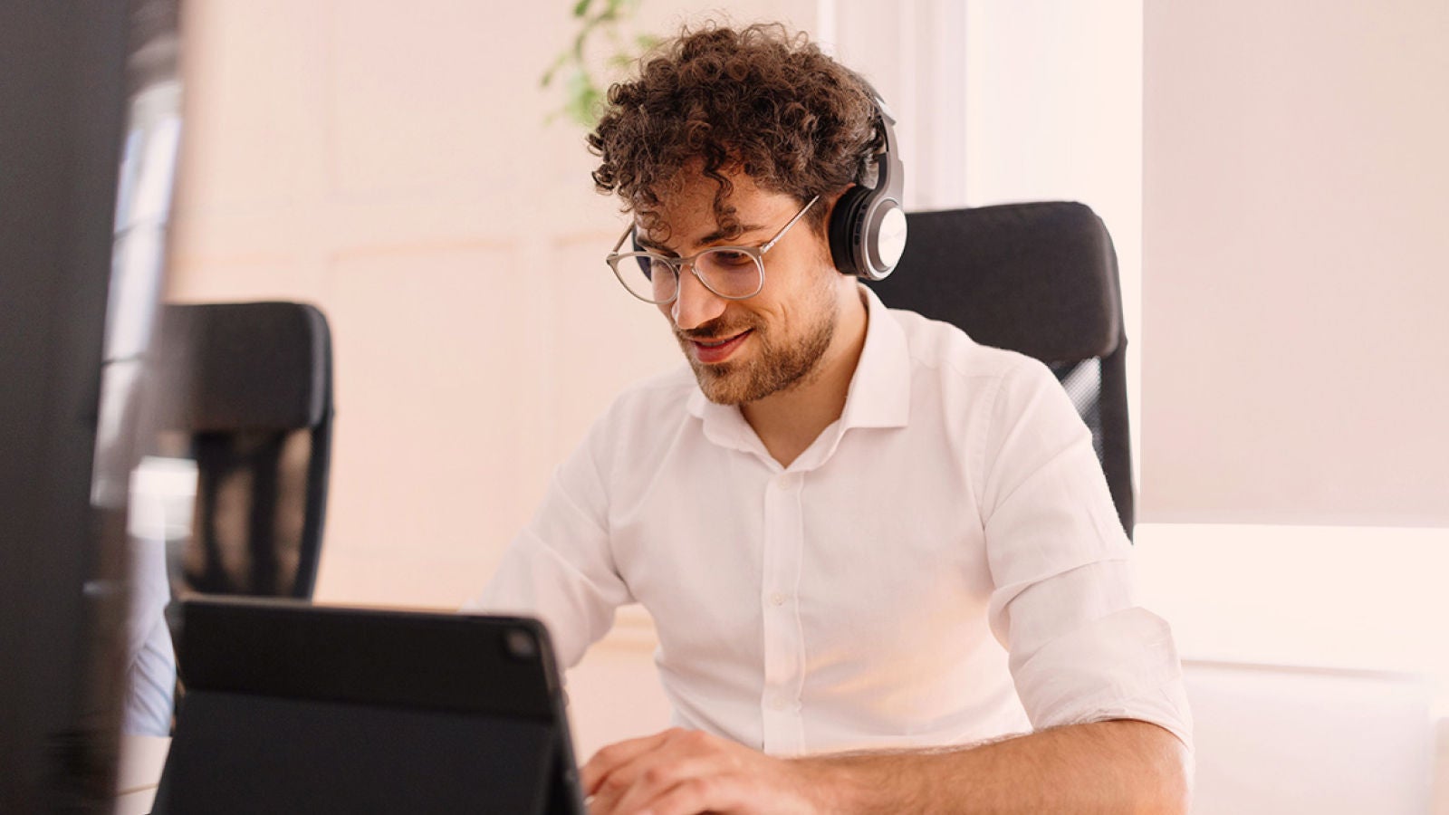 Man wearing headphones working on a tablet at a desk in an office.