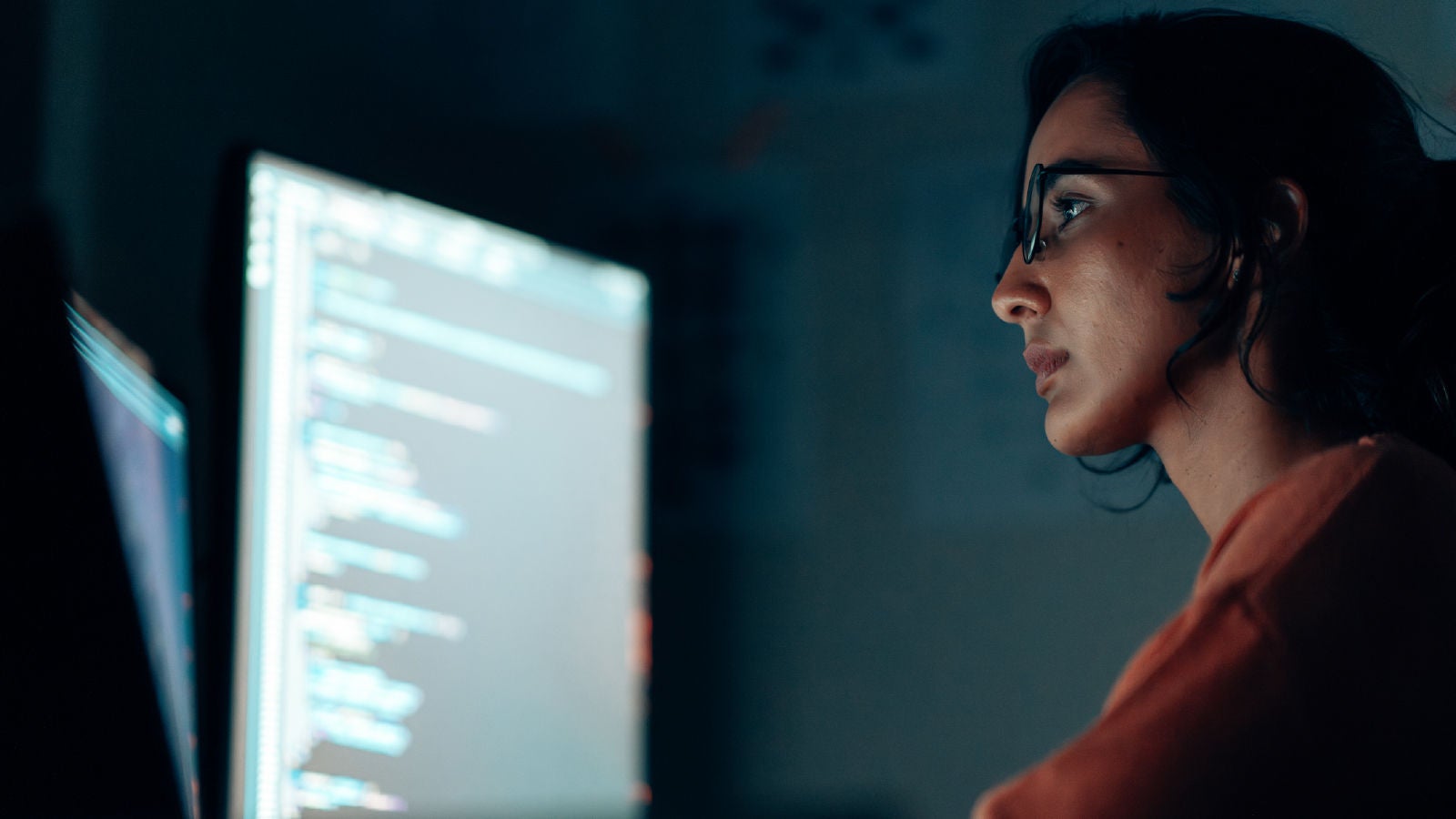 A professional working at a computer workstation, viewing code displayed on a large monitor in a low-light office environment.