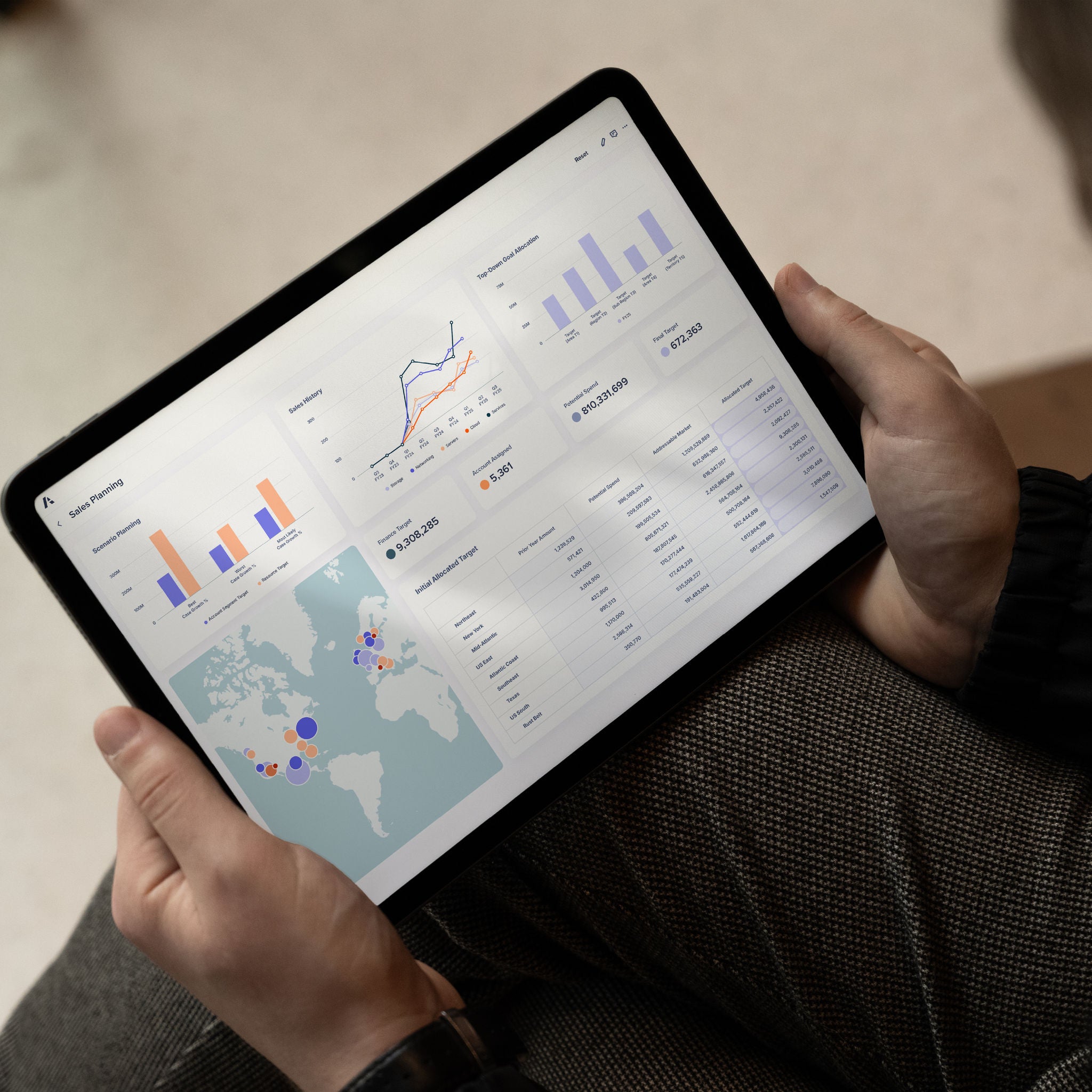 Person holding a tablet displaying a sales planning dashboard with charts, tables, and a map.