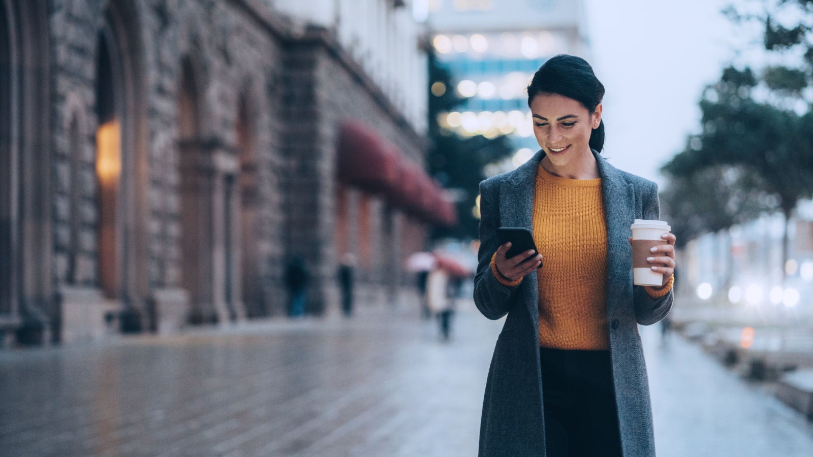 Woman holding a coffee and looking at her cell phone