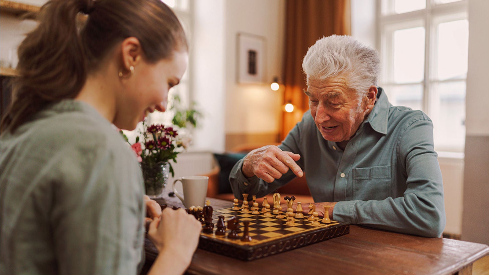 Older man playing chess with a woman in a bright living room.