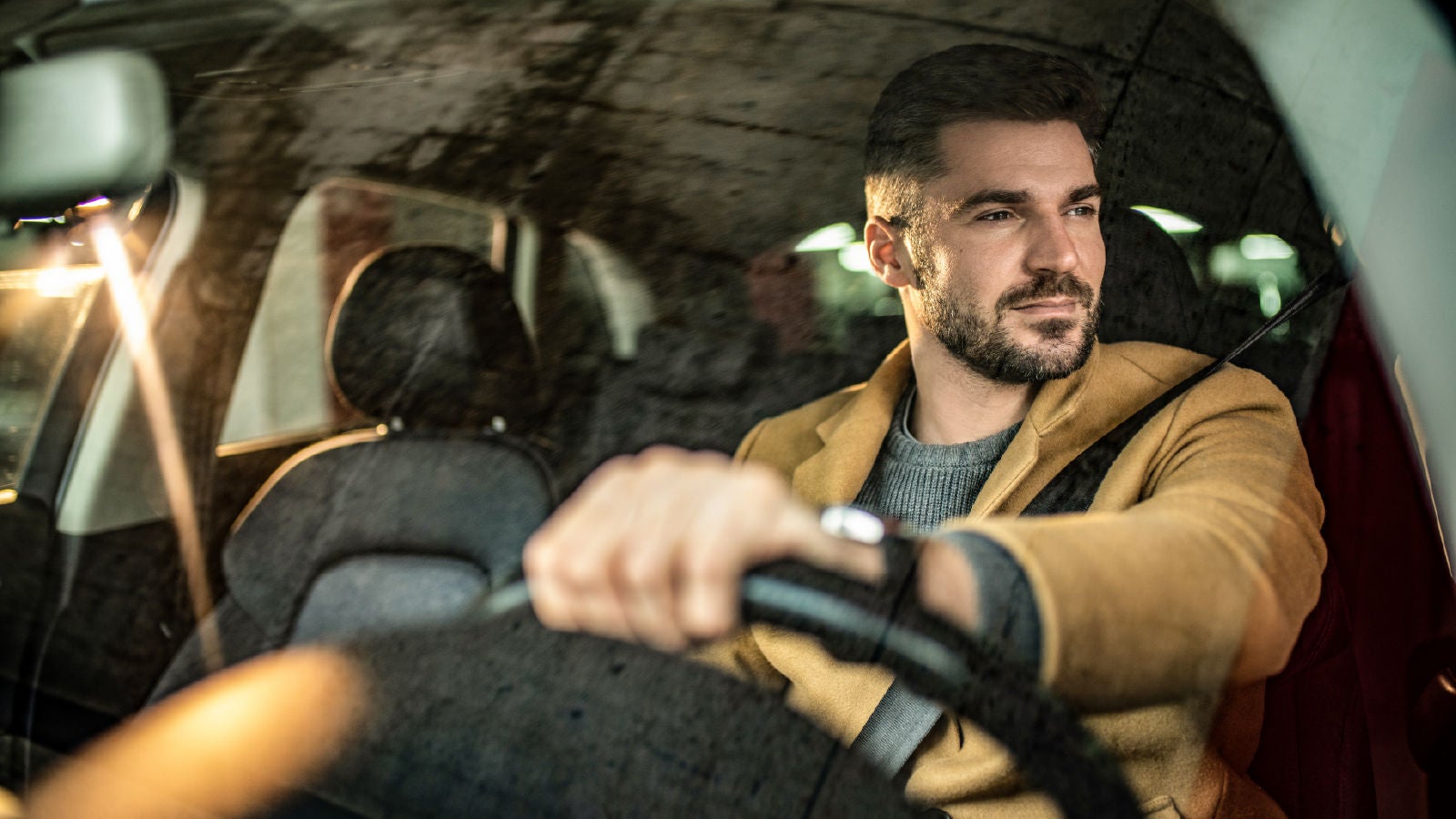 A man driving a car, viewed through the windshield, with focused expression and hands on the steering wheel.