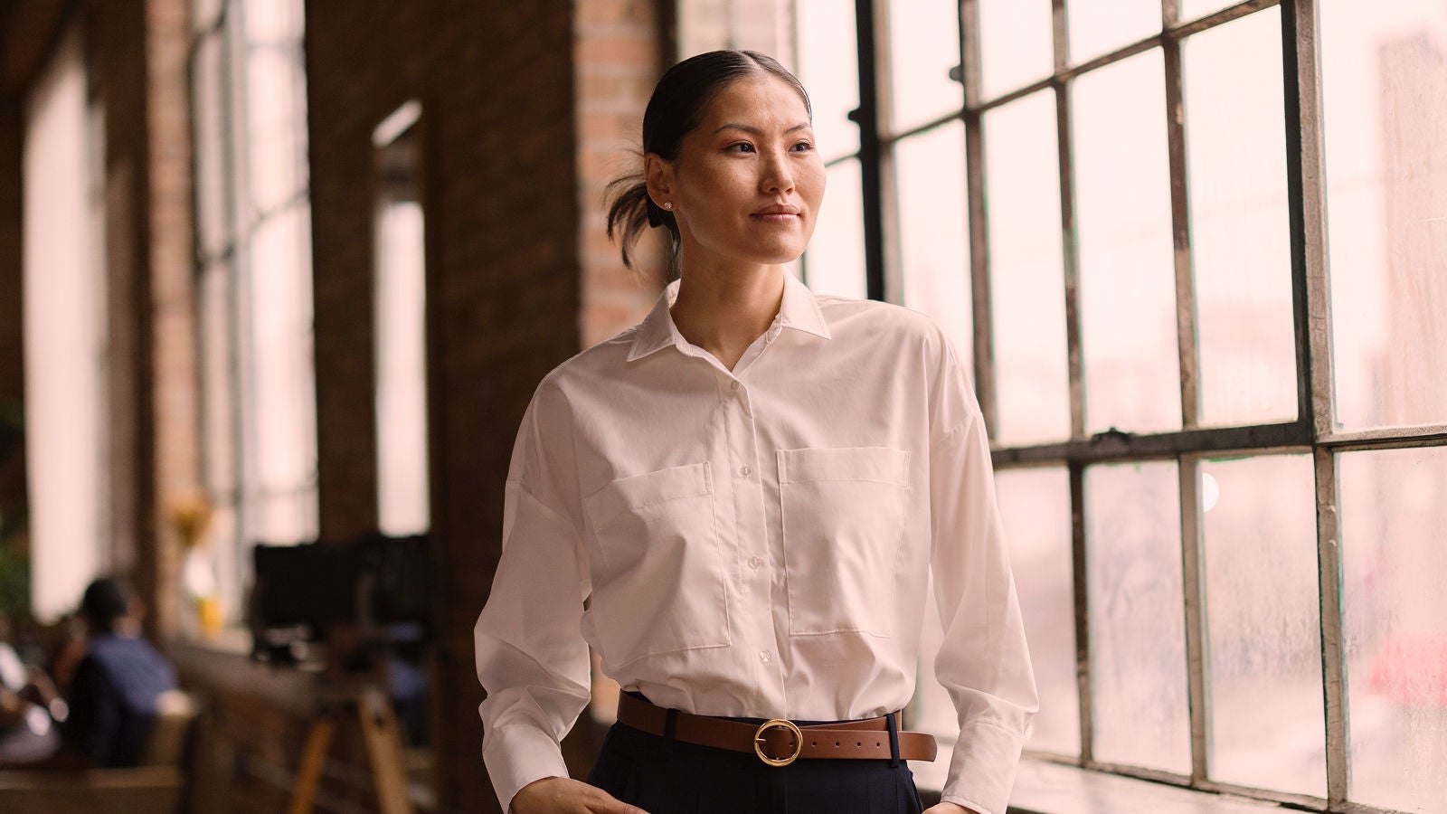 Professional standing beside large windows in an office.