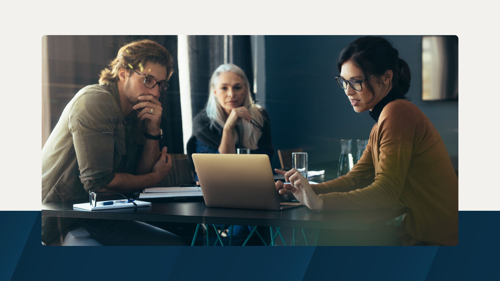 A focused team discussion at a modern table with a laptop, notebooks, and glassware, suggesting collaboration and strategic planning.