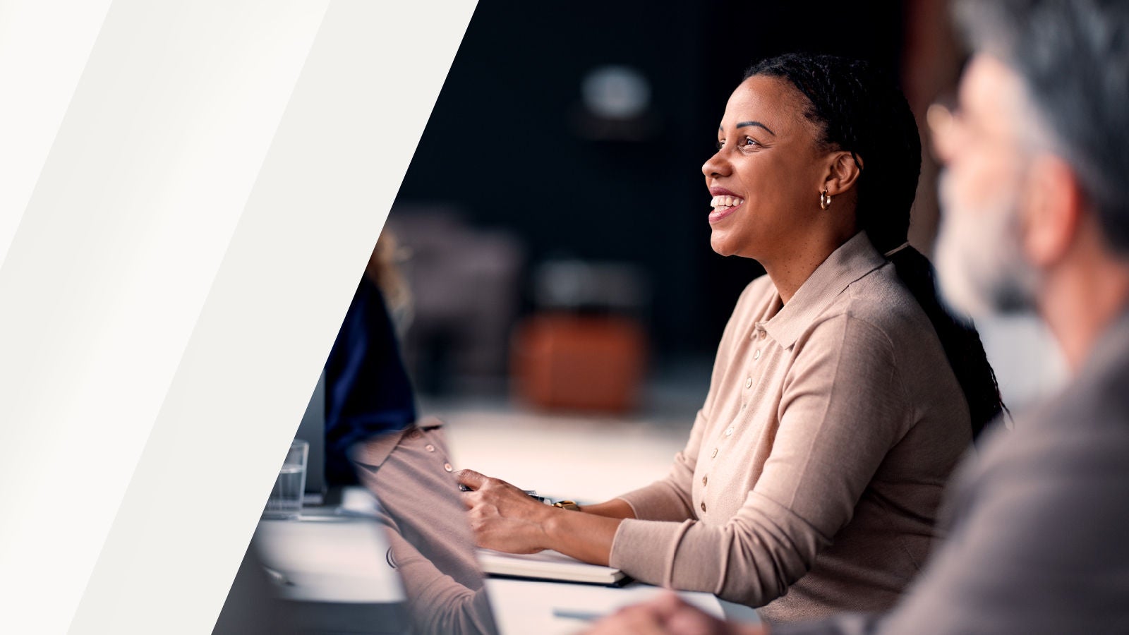 A professional woman smiling and engaging in a meeting with colleagues in a modern office environment.