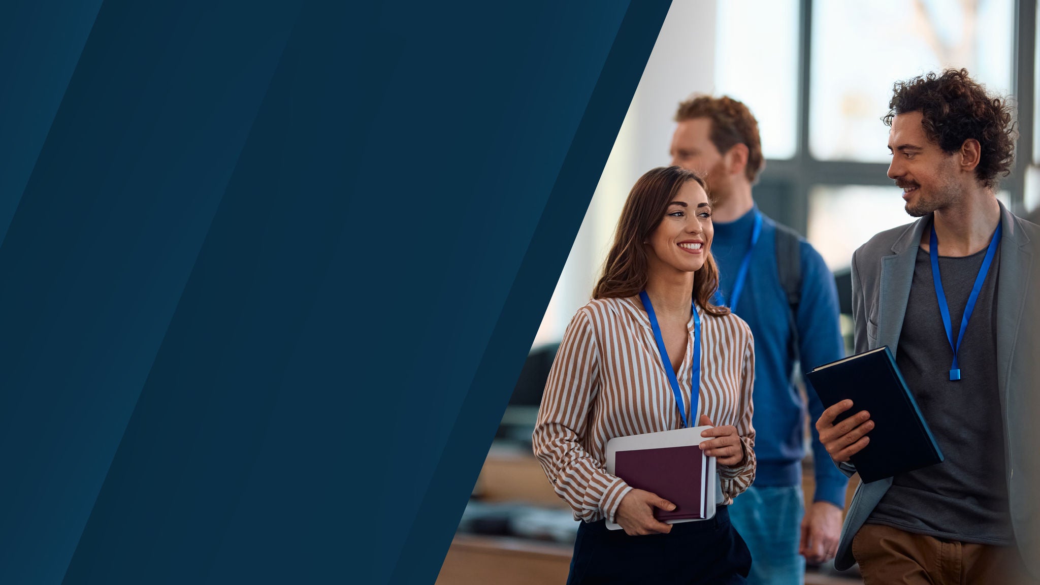Three professionals wearing lanyards walking and talking while holding notebooks in a conference setting.