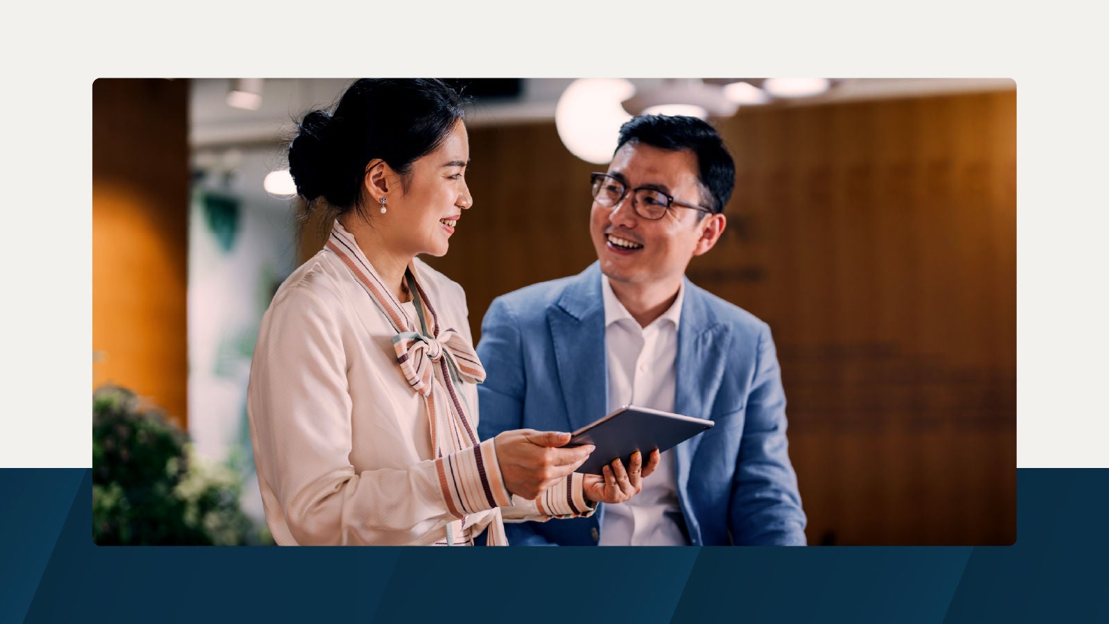 Two professionals in a modern office setting exchanging insights while reviewing a tablet, representing collaborative financial reporting.