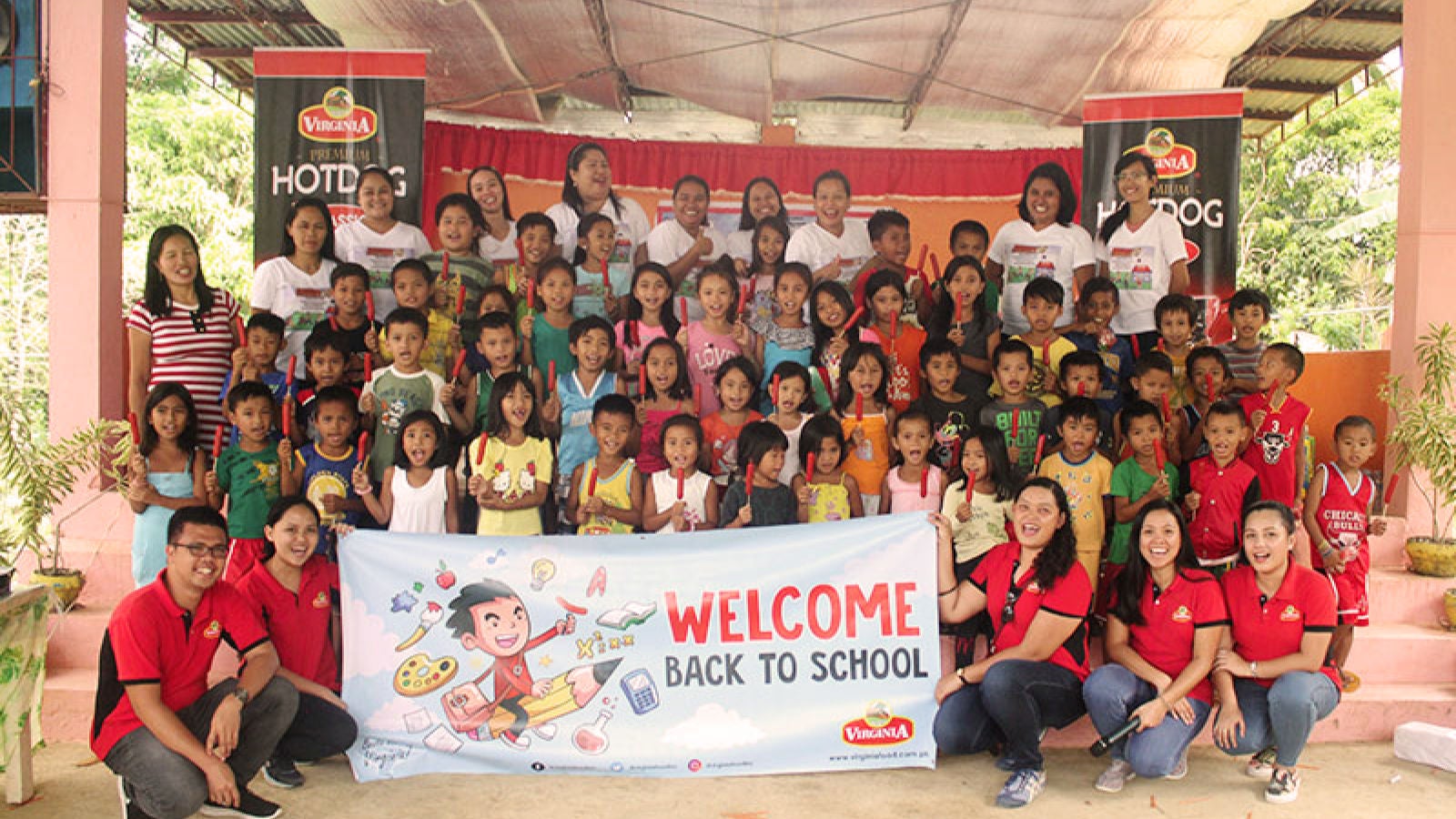 Children and adults gather for a Virginia-sponsored back-to-school event behind a banner reading “WELCOME BACK TO SCHOOL.”