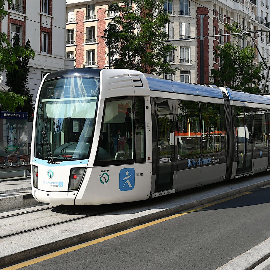 Modern white and blue tram with RATP and Île-de-France Mobilités logos stopped at a city tram station with buildings in the background.